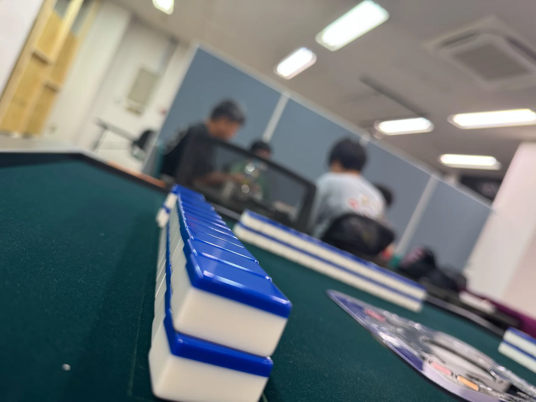 全自動卓の牌と、奥で対局する店内の様子